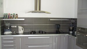 Una cocina moderna con gabinetes grises, estufa a gas, hervidor, licuadora y campana extractora.