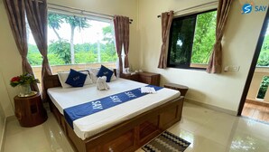 A hotel room with a large bed, a bedside table, a nightstand, and a view of greenery outside. - Say Resort Morning Glory (Mal)