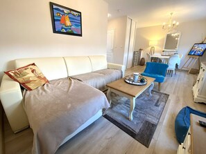 A modern living room with a sofa, a coffee table, and a blue armchair. There is a painting on the wall and a television on a stand. - House with garden 650m from the beach, parking, 2 bedrooms (Perros-Guirec)