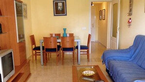 Un soggiorno con divano, televisore, tavolo da pranzo con sedie e tavolino con telecomandi.