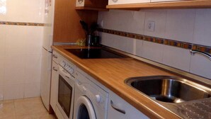 Una cucina compatta con mobili bianchi, un lavello in acciaio inossidabile, forno integrato e lavatrice.