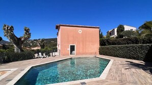 A rectangular swimming pool with a wooden deck surrounding it, a small building with a red roof, and a clear blue sky. - Charming air-conditioned house with pool in La Croix-Valmer (La Croix-Valmer)