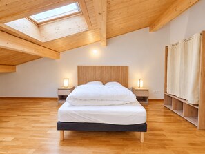 A bedroom with a sloped ceiling, skylight, wooden headboard, two bedside tables with lamps, a bed with white bedding, and wooden flooring. - New apartment for 8, near center, Les Rousses (Les Rousses)