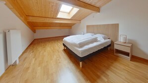 A bedroom with a sloped ceiling, wooden floor, a bed with white bedding, a bedside table, and a nightstand. - New apartment for 8, near center, Les Rousses (Les Rousses)