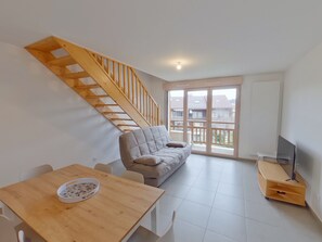 Un salon moderne avec un escalier en bois, un canapé, une table à manger et un meuble pour la télévision.