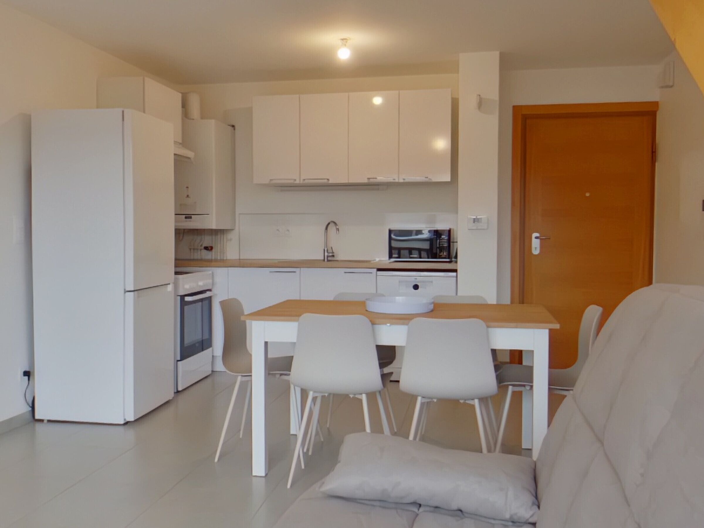 A compact kitchen with white cabinets, a microwave, and a sink. There is a dining table with four chairs and a sofa in the living area.