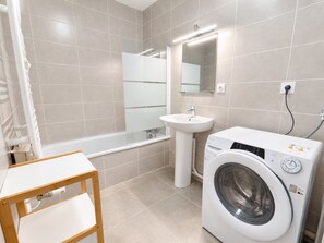 A modern bathroom with a bathtub, sink, and front-loading washing machine. - New apartment for 8, near center, Les Rousses (Les Rousses)