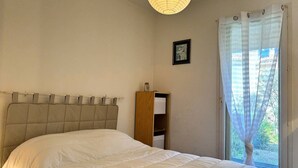 Ein Schlafzimmer mit einem Bett, einem Nachttisch, einem Holzkasten, einer Deckenleuchte und einem Fenster mit Vorhängen.