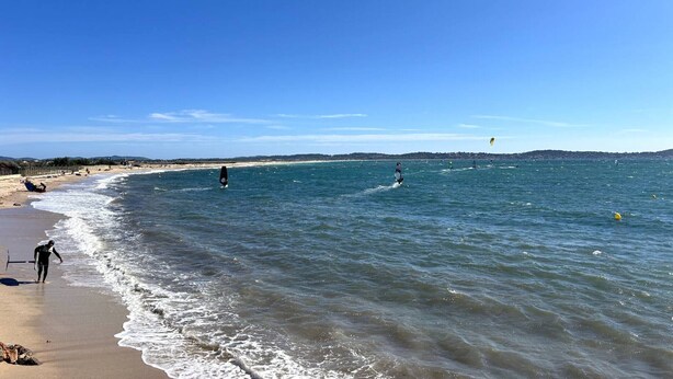 Ein Strand mit blauem Himmel, ruhigem Wasser und sanften Hügeln im Hintergrund.