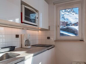A kitchen with white cabinets, a coffee maker, a microwave, and a window with a snowy mountain view. - Ski-in/ski-out apartment Val Thorens - 6 people, central and convenient (Val Thorens)