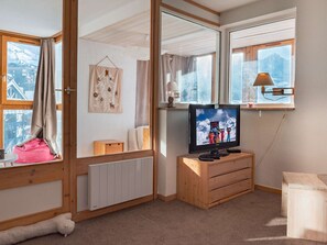 A cozy room with a wooden cabinet, a television, and a window with a view of snow-capped mountains. - Ski-in/ski-out apartment Val Thorens - 6 people, central and convenient (Val Thorens)