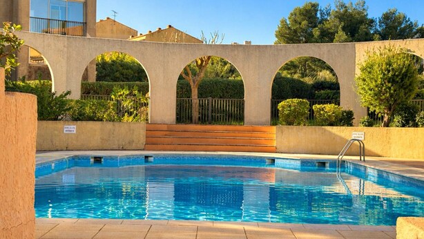 En swimmingpool med klart, blåt vand, omgivet af en betondæk og en lav mur med buer.