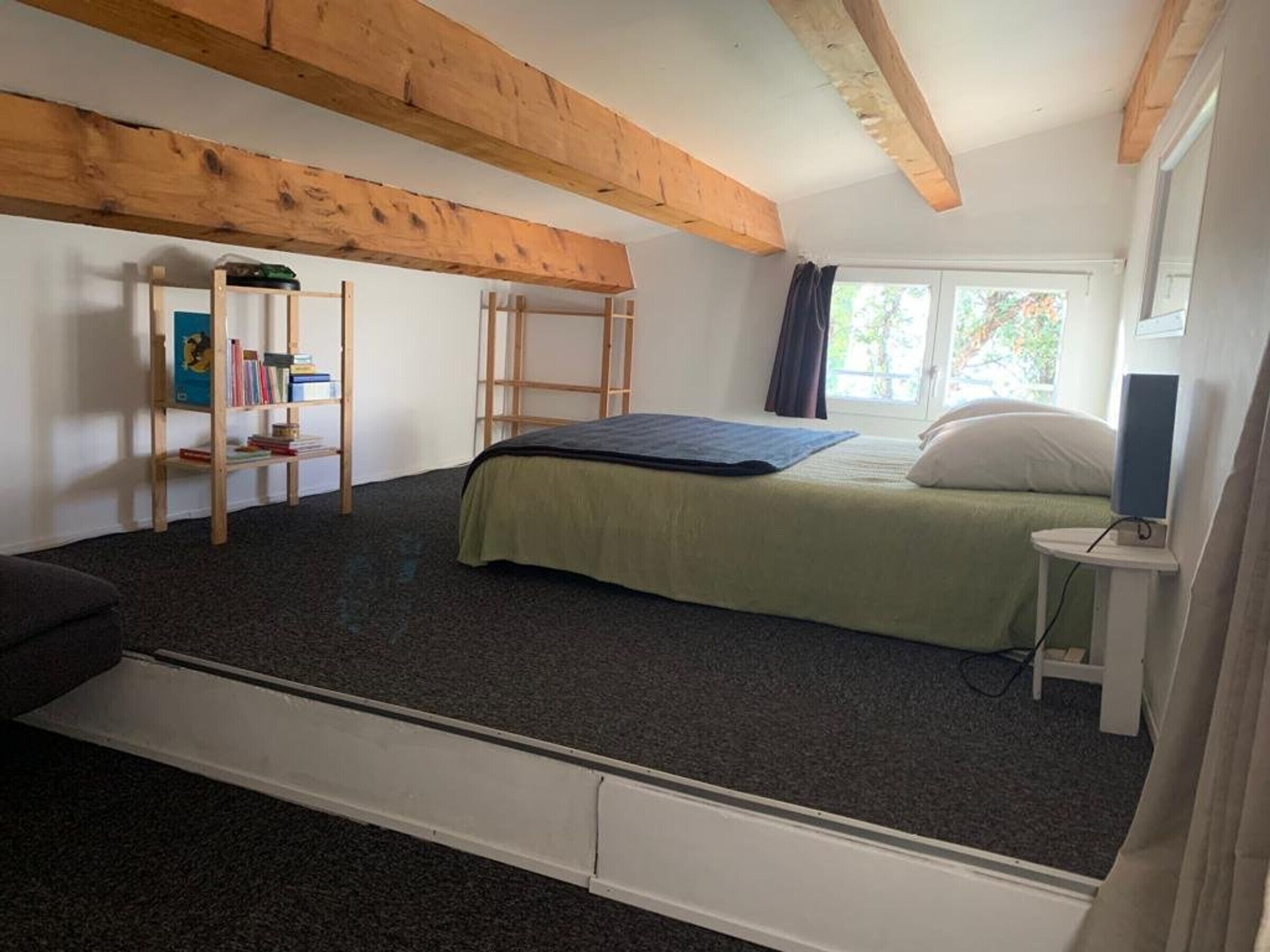 Ein Schlafzimmer mit Etagenbett, kleinem Schreibtisch mit Stuhl, Bücherregal und einem Fenster mit Vorhängen.