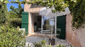 Eine Terrasse mit Tisch und Stühlen, einem weißen Sonnenschirm und Blick ins Innere durch eine Glastür.