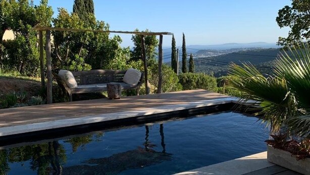 Ein Pool mit Holzterrasse, eine Pergola mit Sitzgelegenheiten und Blick auf die Landschaft.