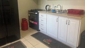 Cocina compacta con armarios blancos, refrigerador negro, estufa a gas, microondas y cilindro de gas rojo.