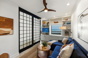 Ein modernes Wohnzimmer mit einem blauen Sofa, einem Holztisch und Meerblick durch ein großes Fenster.