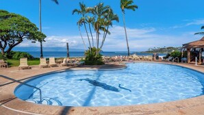A swimming pool with clear blue water, surrounded by lounge chairs and palm trees, with a view of the ocean and a building in the background. - Walk to Beach and Dining + AC - Napili Shores D224 - Updated Studio (Lahaina)