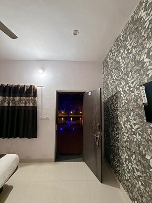 A room with a bed, a door leading to a balcony, and a wall with a floral pattern. - Bliss Resort (Udaipur)