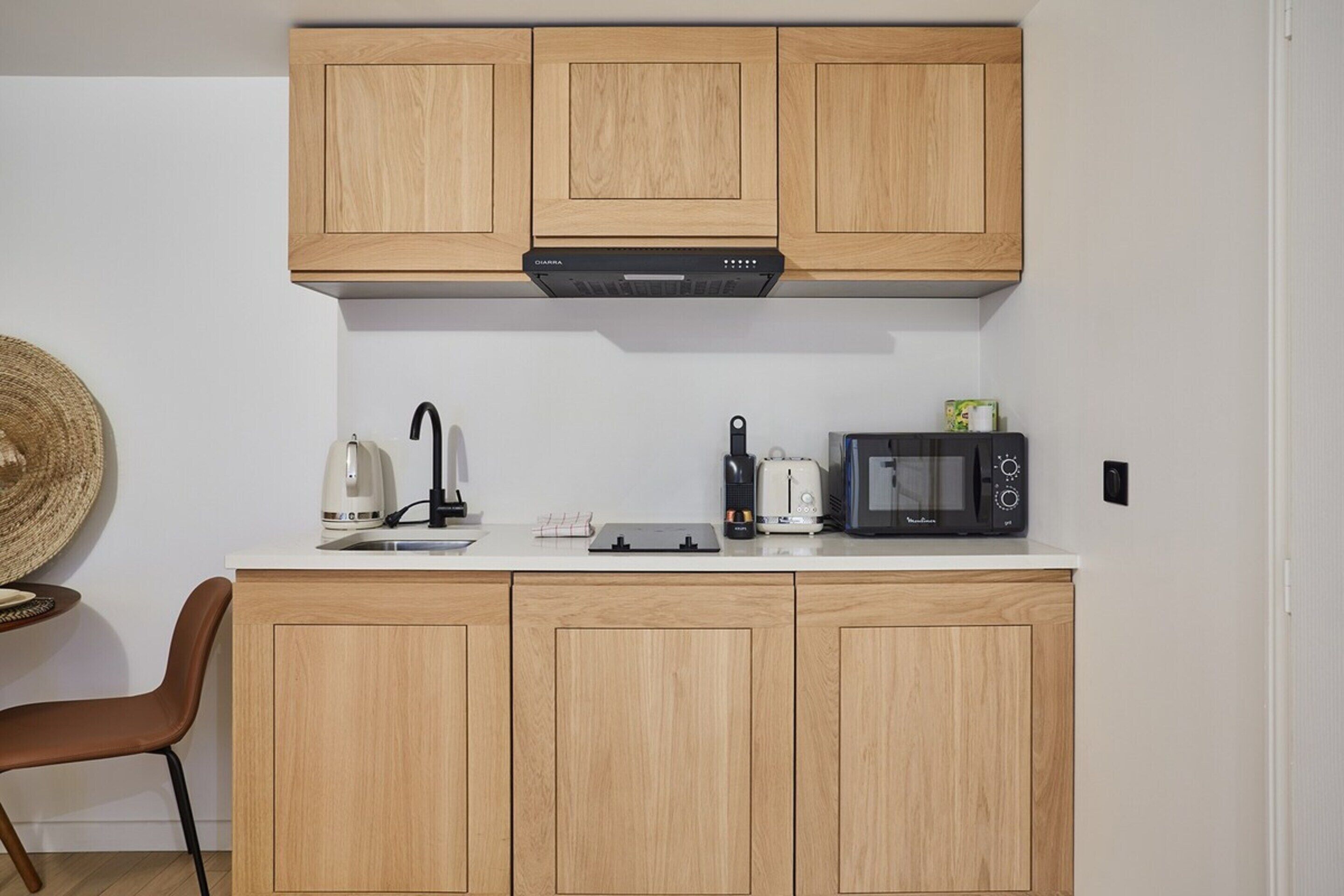 A compact kitchen with wooden cabinets, a microwave, a kettle, and a toaster.
