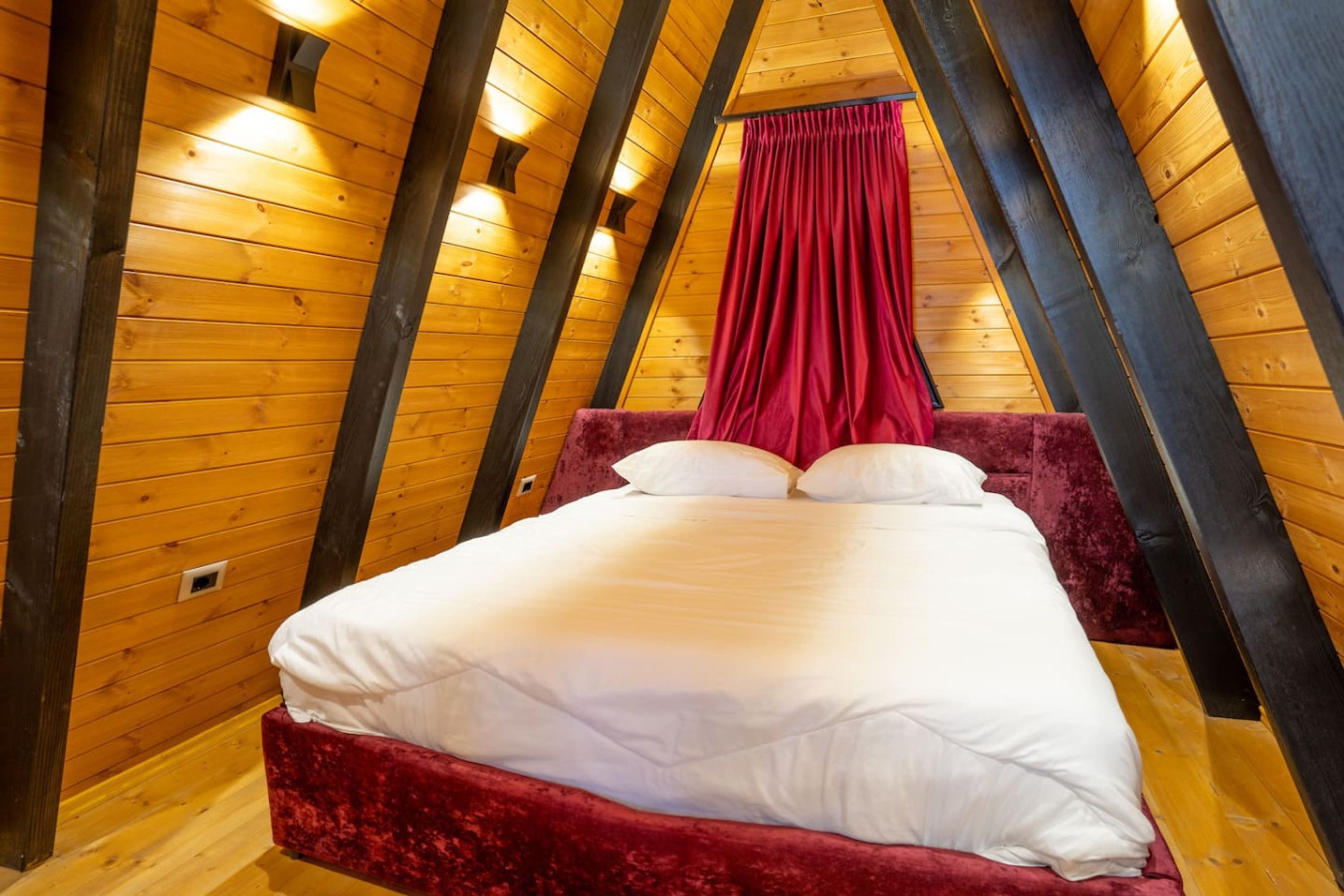 A bedroom with a wooden ceiling, a red velvet bed, and a red curtain.
