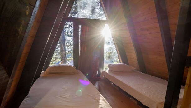 A cozy attic bedroom with two beds, wooden beams, and a view of trees through a window. - Velvet Retreat The Golden Cabins With Garden (Gjinar)