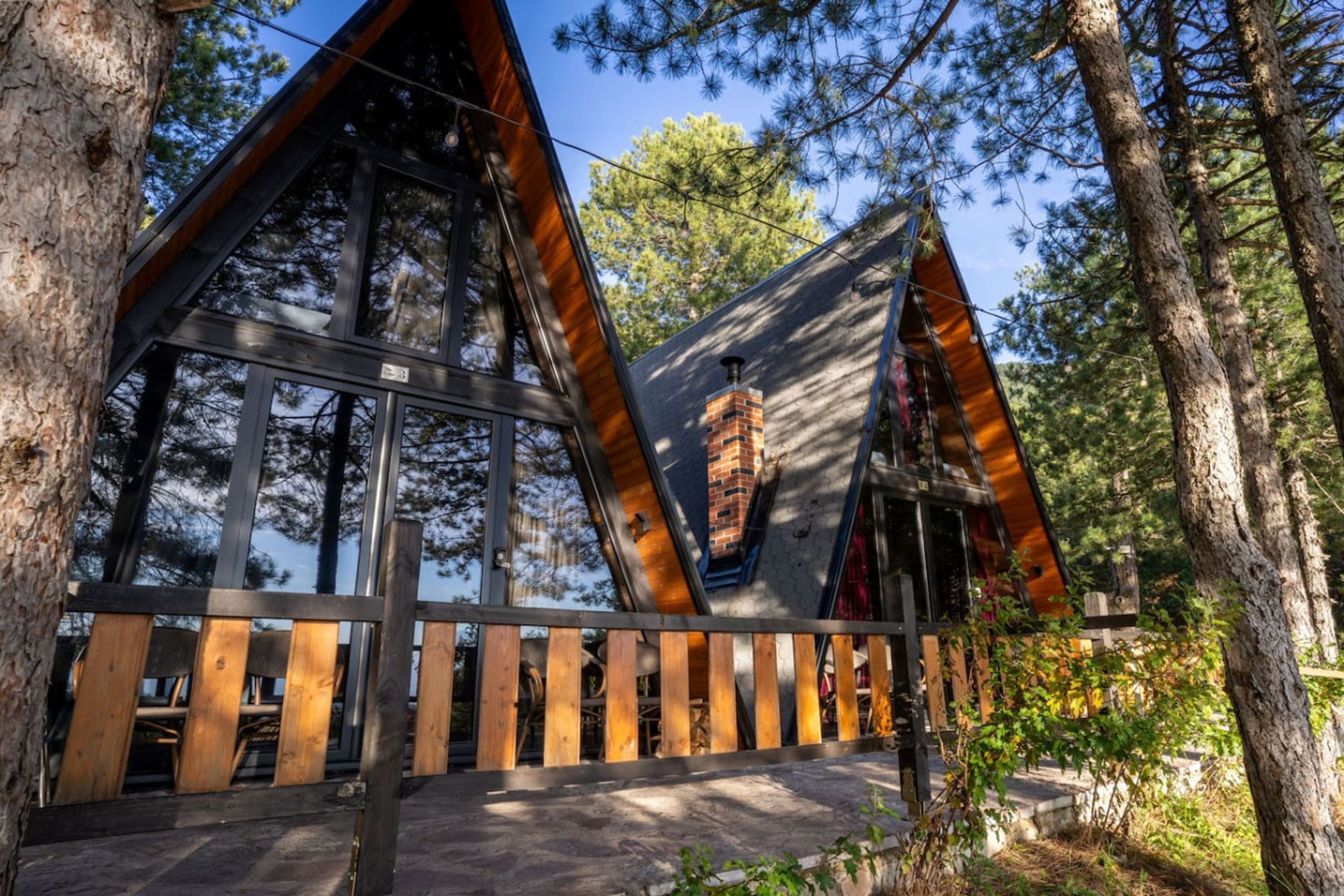 A cabin with large windows, a wooden deck, and a chimney.