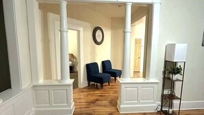 A room with a wooden floor, white walls, a large window, and a door leading to another room.