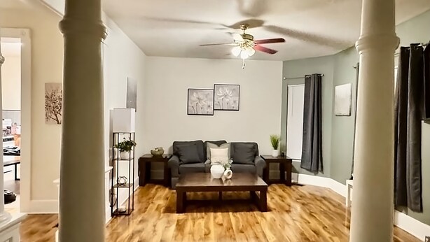 A living room with a wooden floor, a gray sofa, a coffee table, and a ceiling fan.