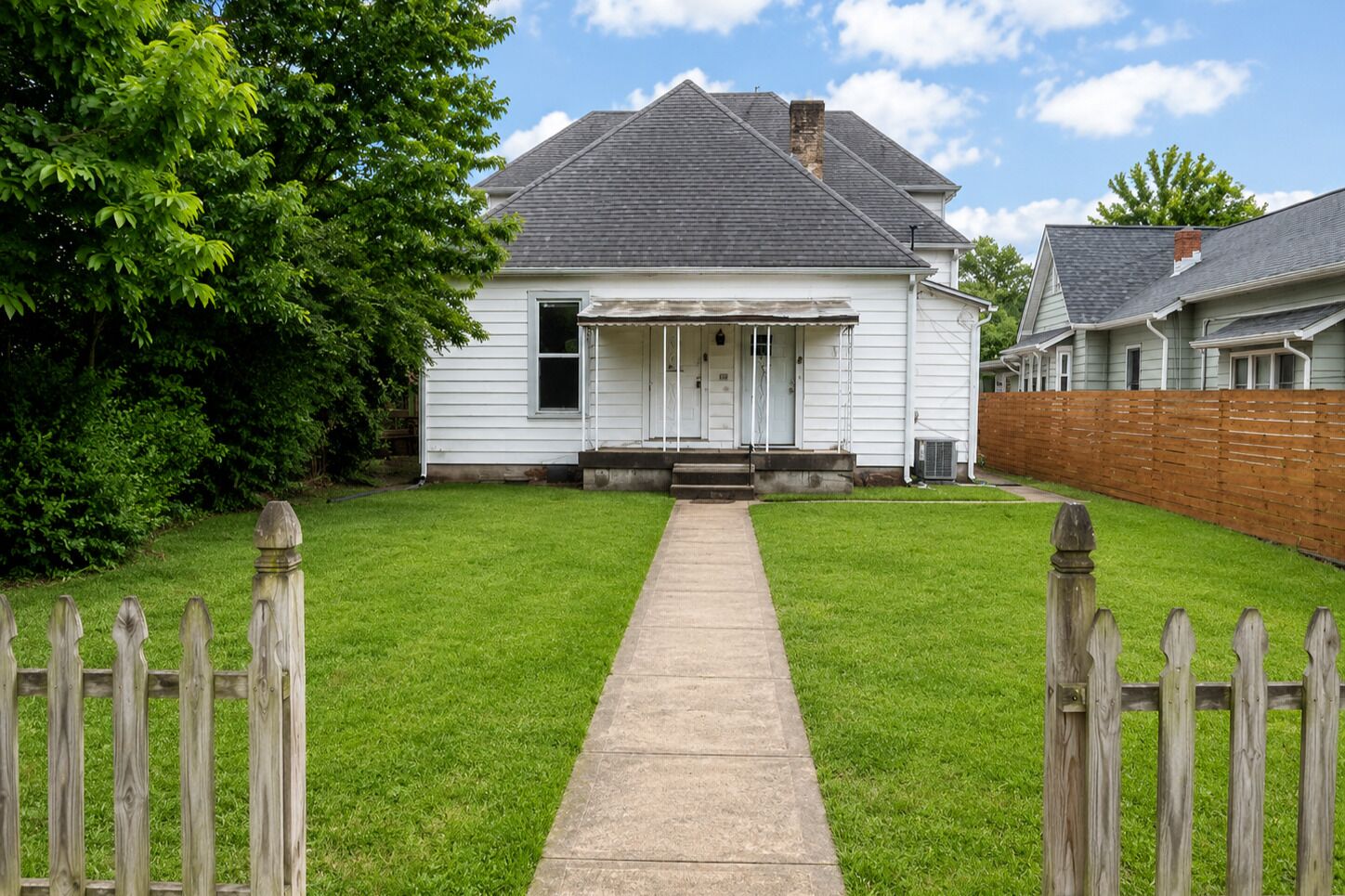 A single-story house with a front porch, a wooden fence, and a well-maintained lawn.