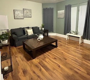 Una sala de estar con una mesa de centro de madera oscura, un sofá y una mesita blanca con una planta.