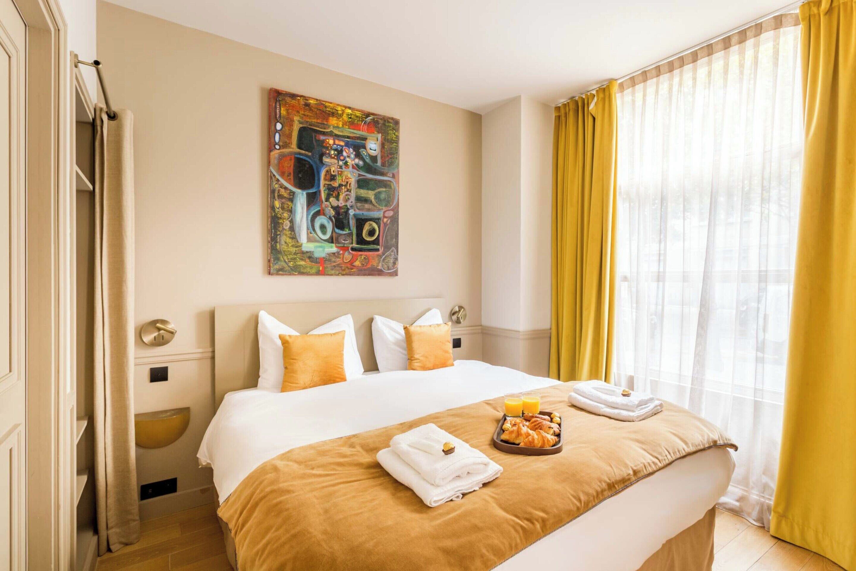 A hotel room with a large bed, a painting on the wall, and a breakfast tray on the bed.