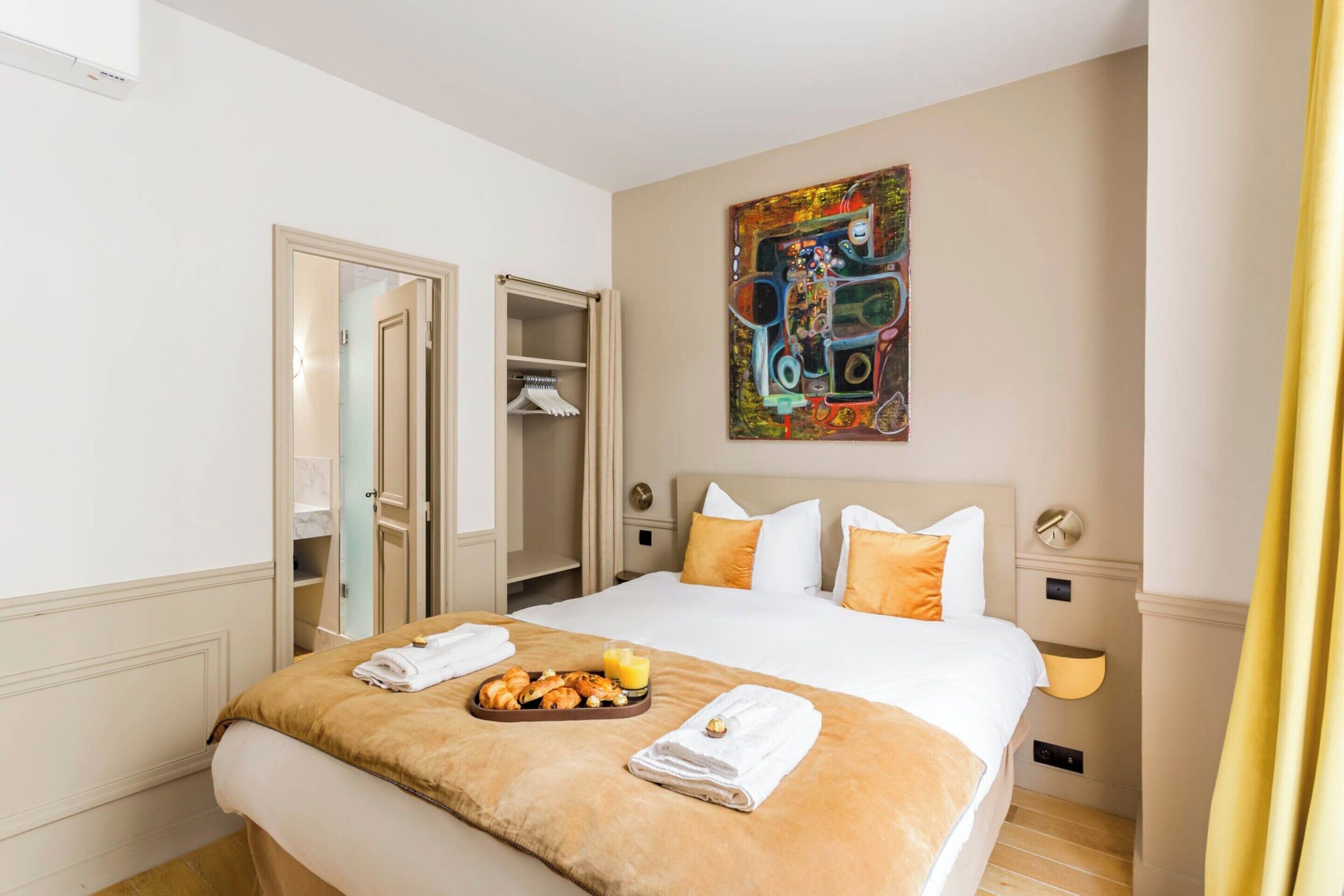 A hotel room with a large bed, a breakfast tray, a painting on the wall, and a wardrobe.
