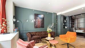 A modern living room with a brown sofa, a pink chair, an orange armchair, and a coffee table. There is a painting on the wall and a floor lamp. - Place des Vosges, Apartment With Air Conditioning (Paris)