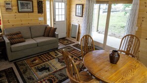 Interior acolhedor de uma cabana, com sofá, mesa de jantar, cadeiras e ventilador de teto.