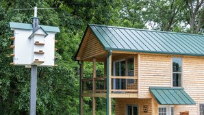 Uma cabana de toras com telhado de metal verde, uma varanda e uma placa com a inscrição 'Cabin #8'.