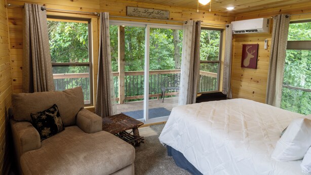 Quarto de cabana de madeira com cama, sofá e uma pequena mesa. Há uma porta de vidro deslizante que dá para um deck externo.