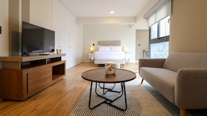 A modern hotel room with a flat-screen TV, a wooden entertainment unit, a round coffee table, a sofa, and a bed with a headboard. - w Engaging Loft in the Heart of San Isidro (Lima)