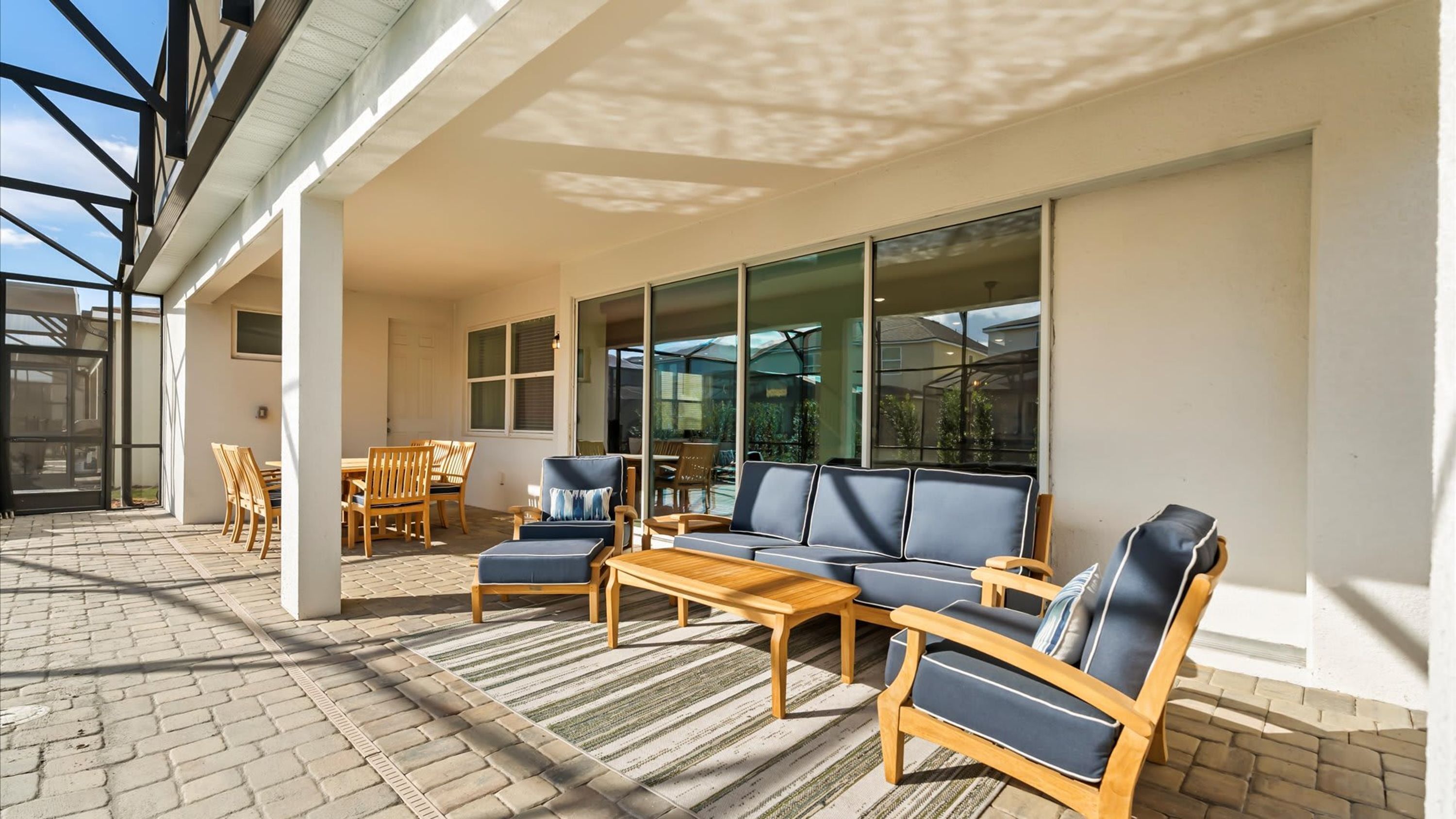 A covered outdoor seating area with a sofa, chairs, and a table, connected to a building with large windows.
