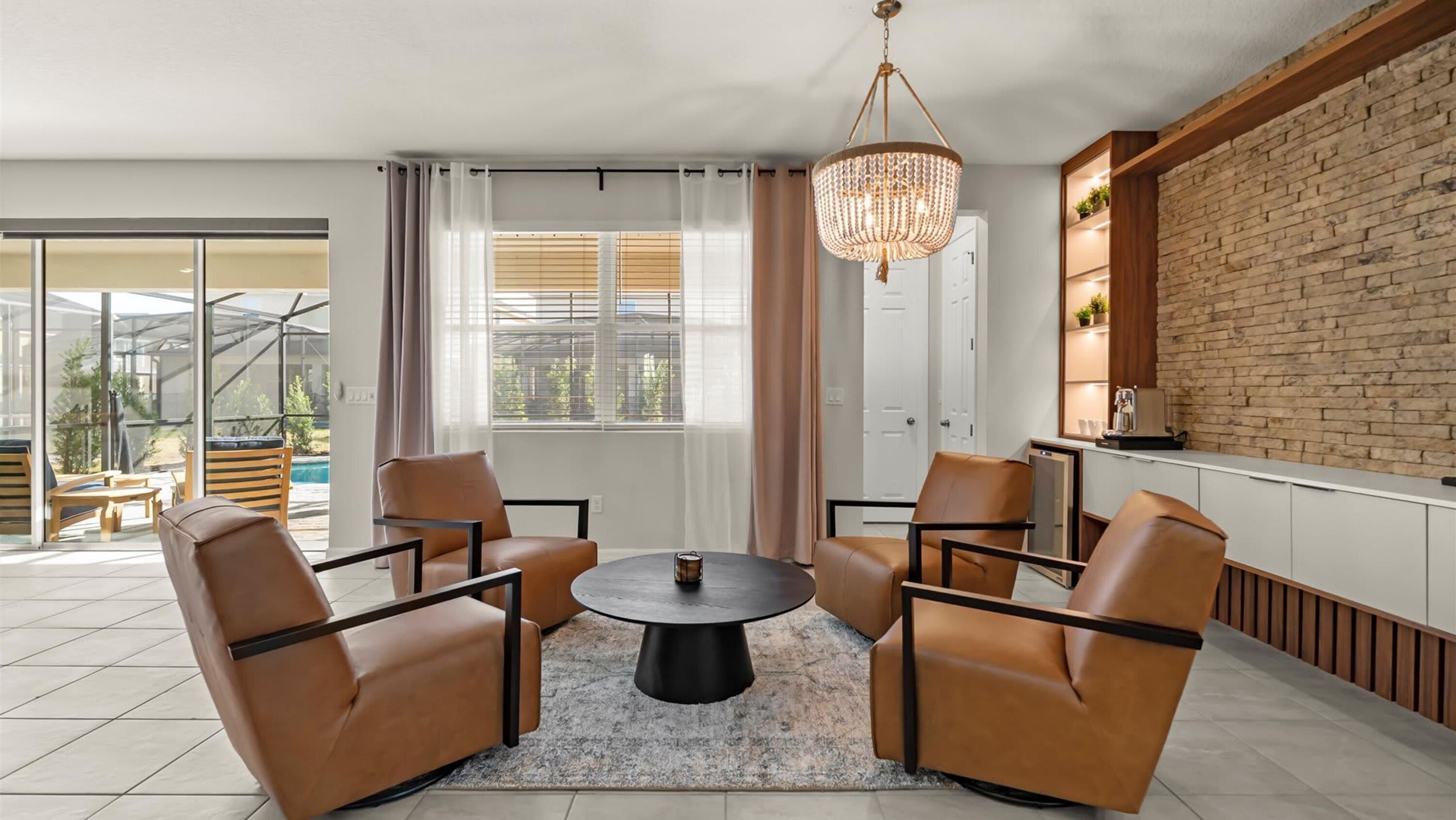 A modern living room with a round table, leather chairs, a chandelier, and a brick wall.