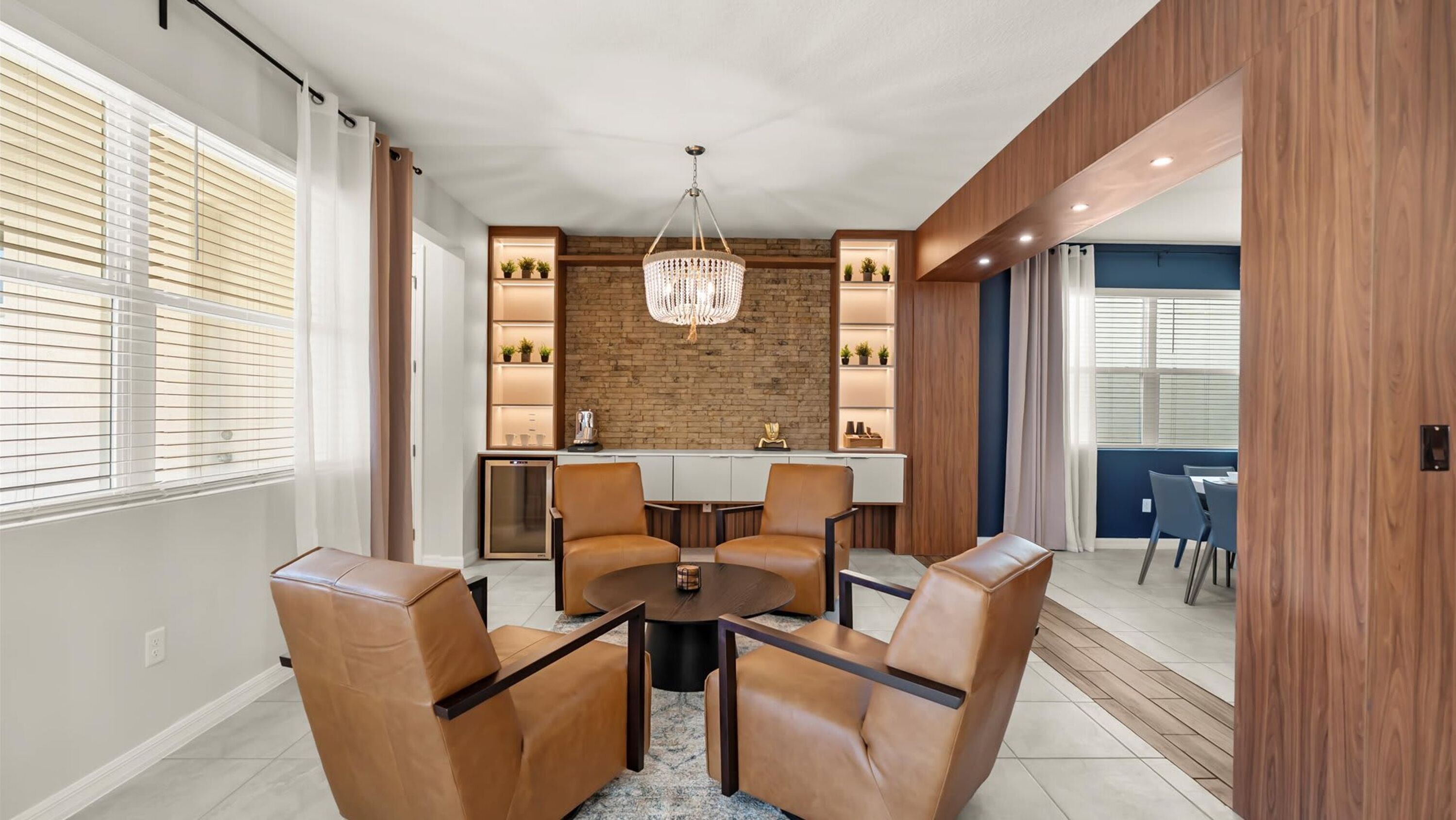 Un comedor moderno con una mesa redonda y sillas de cuero, una araña y una pared de ladrillo decorativa.