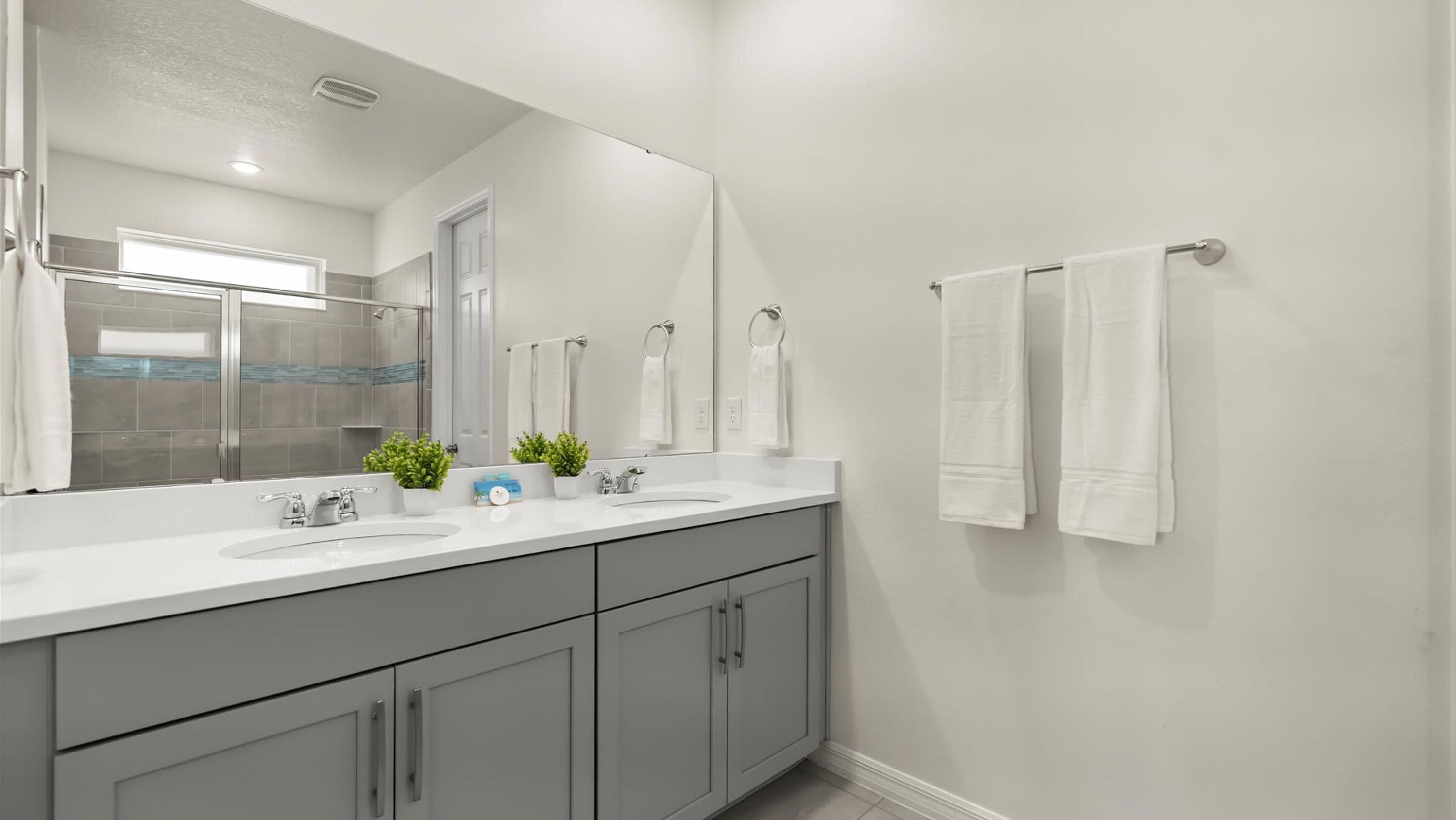 A modern bathroom with a large mirror, two sinks, and a shower.