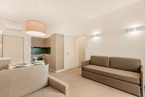 Ein modernes Wohnzimmer mit einer Couch, einem Esstisch für vier Personen, einer Küchenzeile und einem separaten Essbereich.