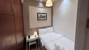 A compact hotel room with a bed, a desk with a lamp, a framed motorcycle picture, and a wardrobe. - Contemporary Partition Room in Tecom  (Dubai)