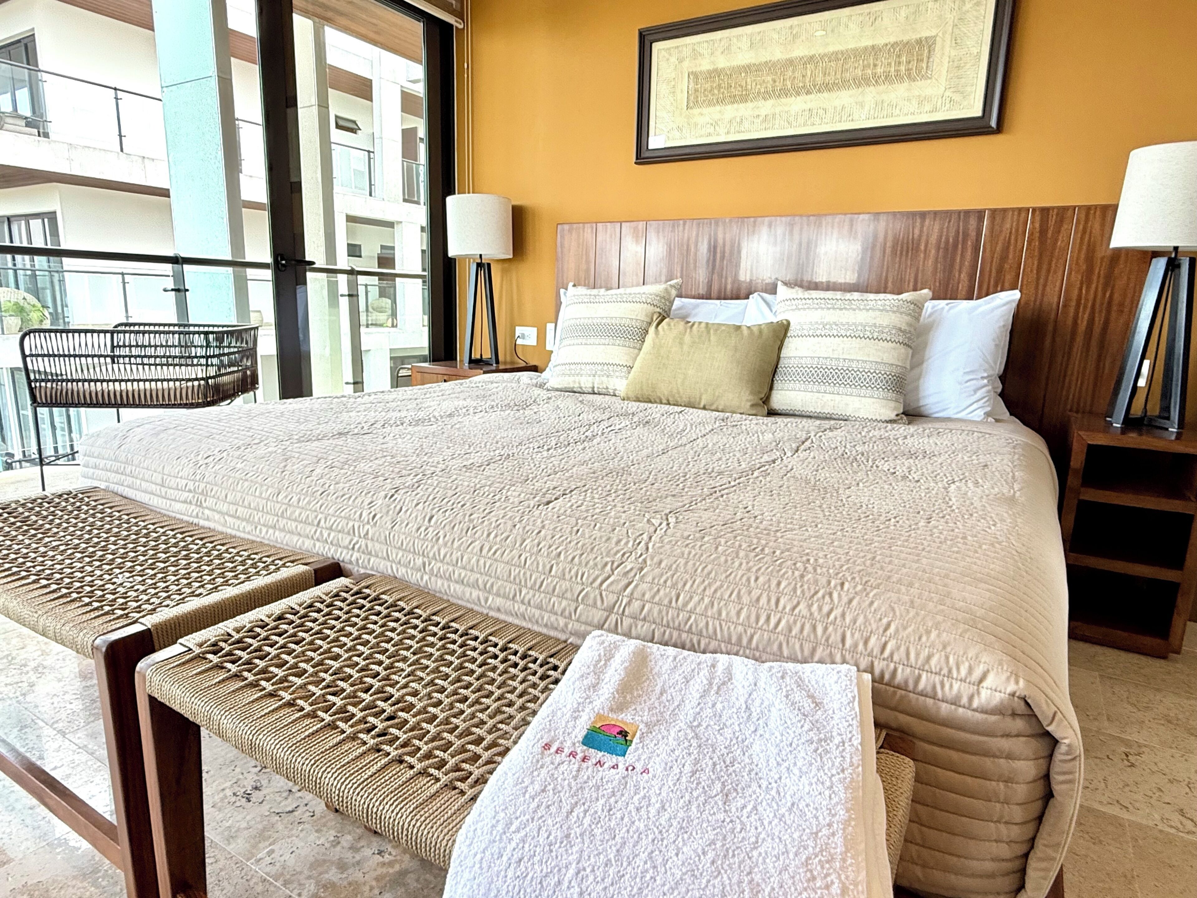 Une chambre d’hôtel avec un grand lit, deux tables de chevet, une chaise et une vue sur le balcon extérieur.