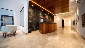 Zona de recepción con mostrador de madera, suelo de mármol y una pared con el letrero 'SERENADA'.