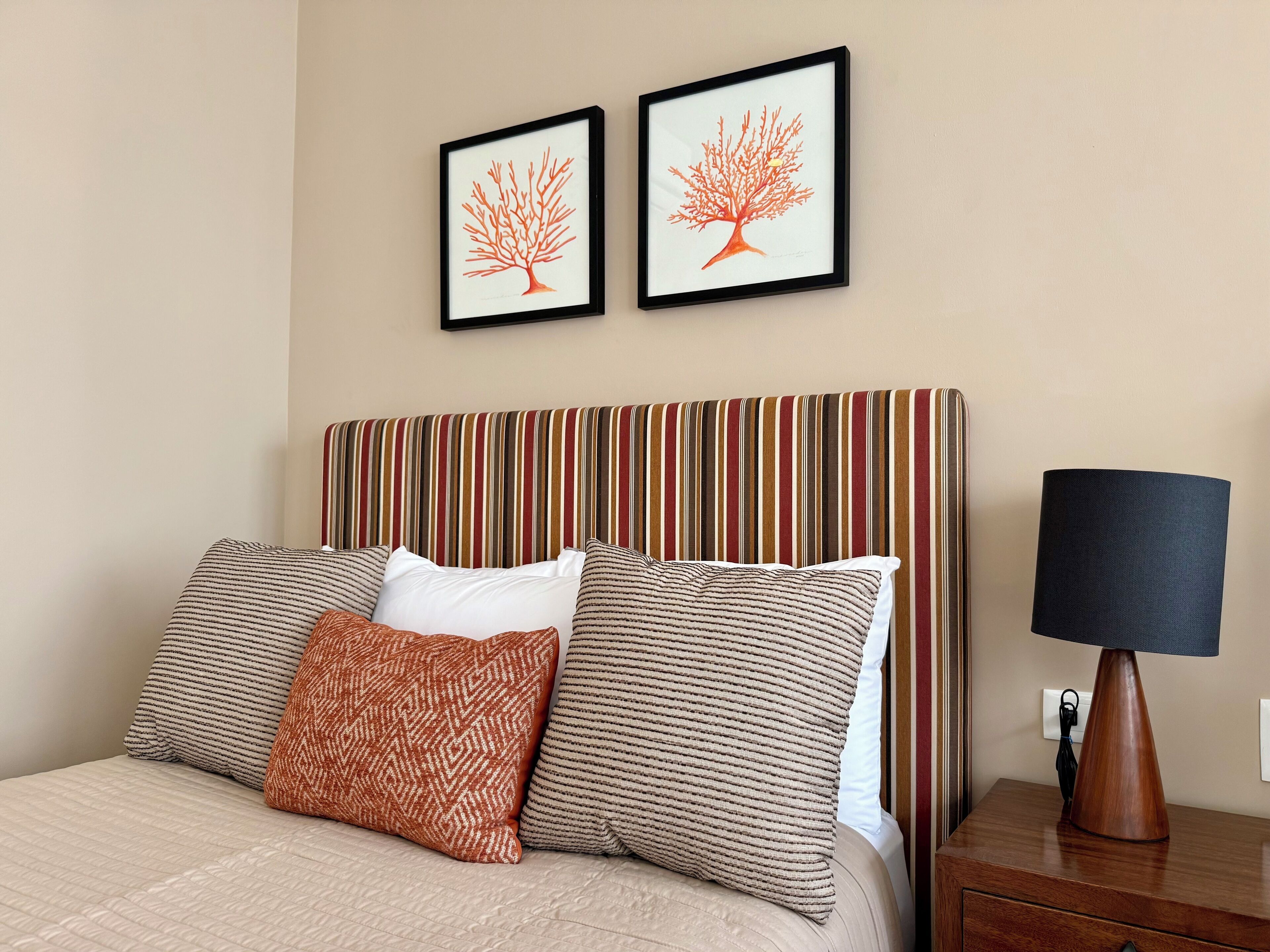 Ein Hotelzimmer mit gestreifter Kopfteil, einem Bett mit gemusterten Kissen und zwei gerahmten Kunstwerken an der Wand.