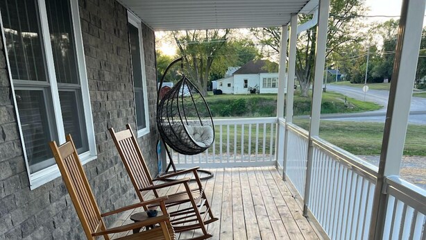 A wooden deck with rocking chairs and a swing chair, overlooking a residential street. - Rathbun Lake, 1.5 miles from the Lake, 2-bdrm, 2 bath sleeps 7 in Rathbun, Iowa (Rathbun)