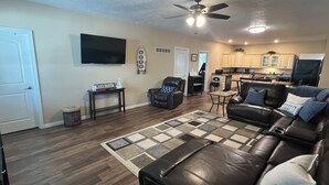 A living room with a leather sofa, a coffee table, a rug, a ceiling fan, and a kitchen in the background. - Rathbun Lake, 1.5 miles from the Lake, 2-bdrm, 2 bath sleeps 7 in Rathbun, Iowa (Rathbun)