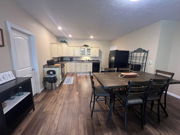 Una cocina compacta con armarios blancos, un refrigerador negro y una mesa de comedor con sillas.